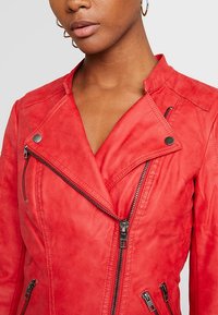 Giacca da moto rossa in pelle con colletto a punta, zip diagonale sul davanti e tasche laterali con zip. Texture morbida con dettagli di cucitura minimi.