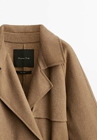 Manteau en laine marron avec large col à revers et étiquette noire visible portant la mention Massimo Dutti à l'intérieur du col arrière.
