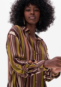 Button-up shirt featuring vertical stripes in green, brown, and cream. Made from a soft fabric with a relaxed fit and single button cuffs.