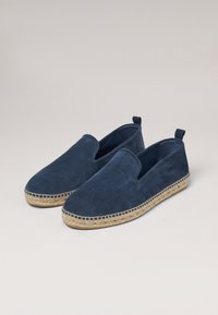 Alpargatas de ante azul marino con suela de cuerda de yute, que presentan un diseño sin hebillas y detalles de costura a lo largo del borde.