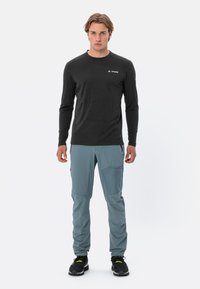 Maglietta nera a maniche lunghe con scollatura a girocollo abbinata a pantaloni grigi chiari a gamba affusolata con tasche laterali, indossati con scarpe nere.