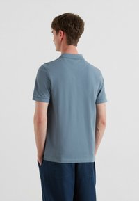 Lichtblauwe polo met korte mouwen, gemaakt van een zachte stof en met een klassieke kraag, gedragen door een model dat met de rug naar de camera staat, gecombineerd met marineblauwe shorts.