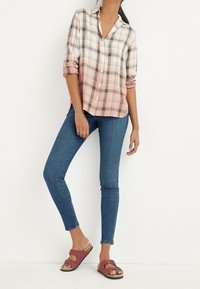 Rutet knap-up skjorte i pink og hvid, opadvendte ærmer, parret med blå skinny jeans og burgunder slip-on sandaler med spænde.