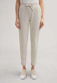 Hellgraue, tapered Sweatpants mit elastischem Bund, Kordelzug und aufgerolltem Saum, kombiniert mit weißen Sneakers. Weicher Stoff.