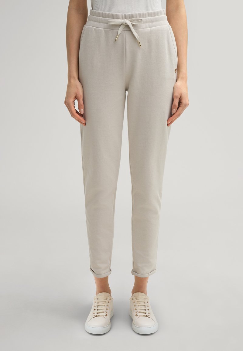 Hellgraue, tapered Sweatpants mit elastischem Bund, Kordelzug und aufgerolltem Saum, kombiniert mit weißen Sneakers. Weicher Stoff.