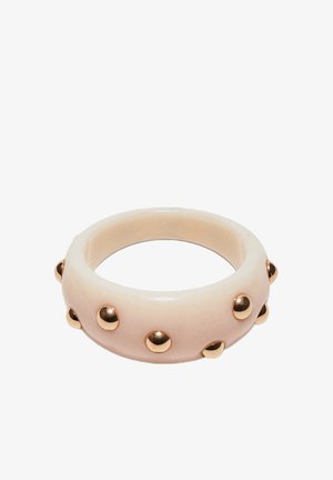 Bracciale rigido beige spesso con borchie rotonde dorate distanziate uniformemente sulla sua superficie esterna.