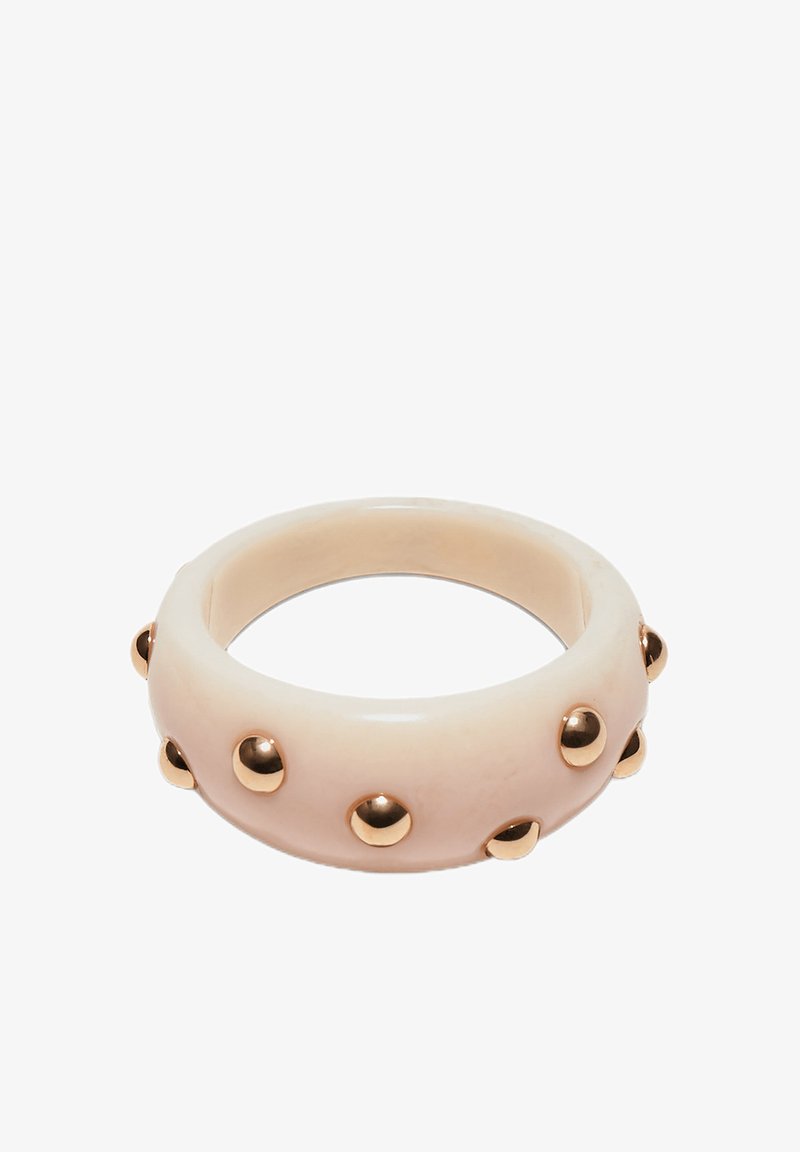 Bracelet manchette beige avec des clous ronds dorés uniformément espacés sur toute sa surface extérieure.