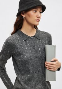Sivi rebrasti kardigan z bleščicami, ovratni zasnova in gumbi spredaj. Ustrezno kombiniran s svetlo sivim pravokotnim reverzibilnim torbico in črnim klobukom vedro.