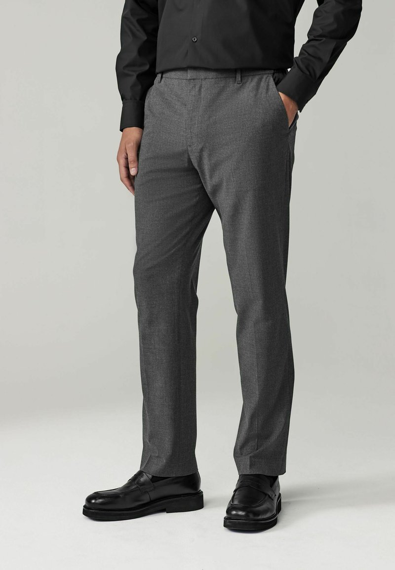 Pantalones de traje grises hechos de una tela ligera, con una textura suave, bolsillos laterales y un ajuste a medida, combinados con zapatos negros.