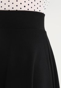 Schwarzer Rock mit einem breiten Bund, aus glattem Stoff. Verfügt über Falten, die von der Taille abfallen und ein gepunktetes Oberteil komplementieren.