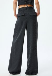 Schwarze Nadelstreifen-Hosen mit weitem Bein und hoher Taille, mit zwei Gesäßtaschen und einer glatten, leichten Stofftextur.