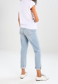 Vitt kortärmad t-shirt, ljusblå jeans med uppvikta ärmar och vita skor med svarta detaljer, sedd bakifrån.