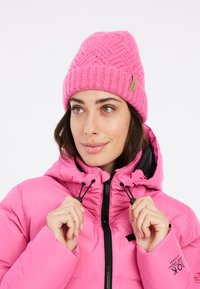 Berretto lavorato a maglia rosa con un motivo texturizzato e un'etichetta con logo. Indossato con un giubbotto trapuntato rosa abbinato, dotato di zip e cappuccio con stringa.