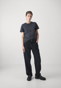 Donkergrijze katoenen t-shirt met een klein logo op de borst, gecombineerd met een losse zwarte broek en stevige zwarte schoenen. Minimalistisch ontwerp.