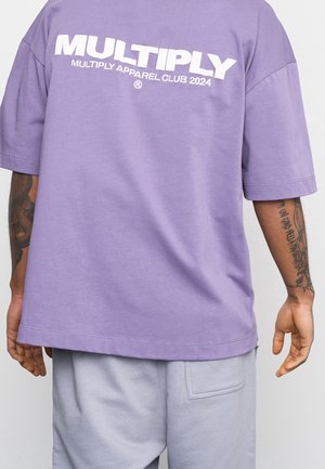 T-shirt oversized violet avec un grand texte blanc "MULTIPLY APPAREL CLUB 2024" au dos. Tissu doux avec une coupe décontractée.