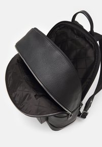 Μαύρο δερμάτινο σακίδιο με λεία επιφάνεια, κλείσιμο με φερμουάρ και επενδυμένο εσωτερικό. Διαθέτει ρυθμιζόμενους ιμάντες και χωρίς ορατές λεπτομέρειες από μέταλλο.