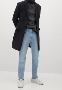 Dunkler Wollmischmantel mit drei Knöpfen, grauer gerippter Rollkragenpullover, hellblaue schmale Jeans und weiße Sneaker. Minimalistisches Design und klassische Farben.