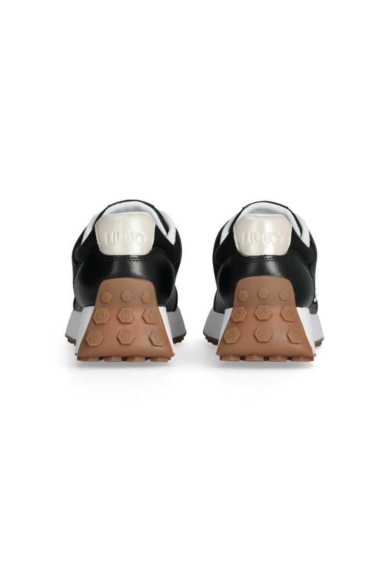 Chaussures de sport noires à design bas, avec une semelle en caoutchouc brun texturé et un accent de talon argenté brillant. Design de semelle intermédiaire blanche.