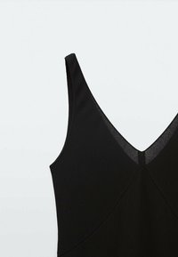 Robe noire sans manches avec un décolleté en V profond, un tissu texturé et une coupe ajustée au design épuré.