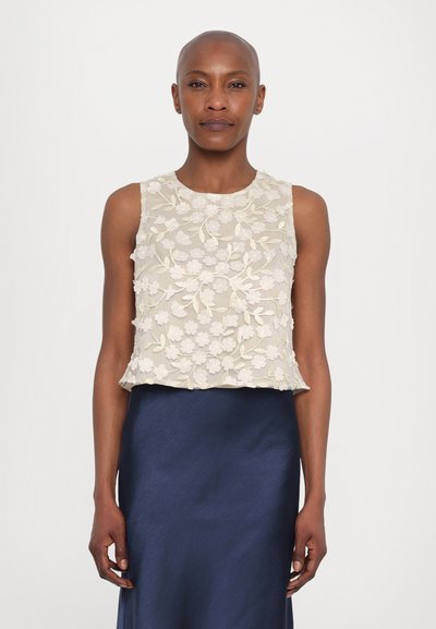 Haut sans manches avec un motif floral brodé en crème sur un tissu transparent, associé à une jupe en satin bleu marine. Texture lisse, forme cropped.