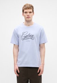 Jasnofioletowa bawełniana koszulka z krótkim rękawem z dużym czarnym, kursywowym logo "Calvin Klein". Klasyczny okrągły dekolt.