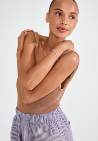 Pruun kudumitega top laiade rihmadega, koos siniste ja valgete triibuliste lühikeste pükstega, mis näitavad lõdva ja tekstuurse disaini.