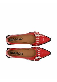 Scarpe slingback in vernice rossa con punta affusolata, dettaglio della fibbia argentata e fori circolari lungo la fascia. Suola nera.