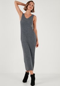 Grey ribbed knit maxi dress with v-neckline and sleeveless design. Paired with black ankle boots, featuring a soft texture and elongated silhouette.