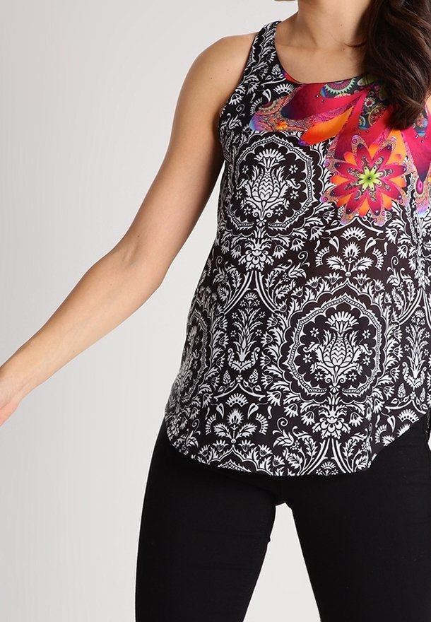 Haut sans manches avec des motifs ornés noirs et blancs et un design floral coloré près de l'encolure, porté avec un pantalon noir.