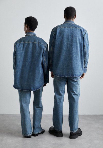 Jachete din denim și blugi asortați în albastru deschis. Jachetele au o croială lejeră, cu cusături vizibile. Încălțămintea este neagră, cu o talpă masivă.