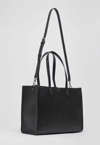 Sac fourre-tout en cuir noir avec deux anses supérieures et une bandoulière amovible, au toucher lisse et au design minimaliste.