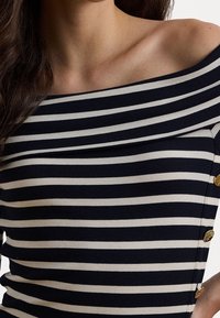 Přiléhavý pruhovaný top s odhalenými rameny v námořnické modré a krémové barvě, s vroubkovanou strukturou a dekoračními zlatými knoflíky na jedné straně.