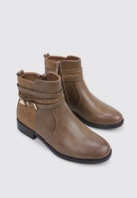 Botas de tobillo de imitación de cuero marrón con un acabado suave, cremallera lateral, correas decorativas y pequeños remaches metálicos en la parte superior. Suela de goma negra.