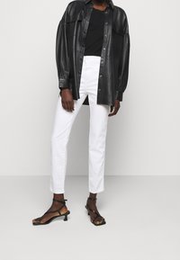 Camisa negra de cuero con botones, parte superior negra ajustada, jeans rectos blancos y tacones negros con tiras y un pequeño tacón cuadrado.