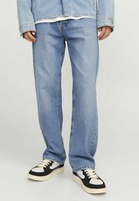Lichtblauwe denim jeans met een relaxte pasvorm en subtiele vervaging, gecombineerd met zwart-witte sneakers met een gemusterd ontwerp.