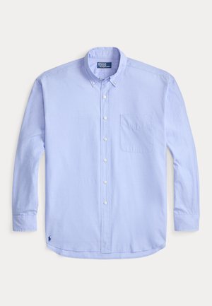 Camisa de manga larga color azul claro con cuello de botón, bolsillo frontal y logo bordado en la parte inferior izquierda. Textura de algodón suave.