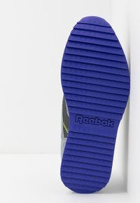 Podošev boty Reebok z fialové gumy s podélnými drážkami. Šedý svršek se šitím v neonově zelené barvě. Jednoduchý, funkční design.