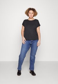 Czarny t-shirt z krótkim rękawem zestawiony z niebieskimi dżinsami o prostym kroju i czarnymi butami, prezentowany na modelu na tle białym.