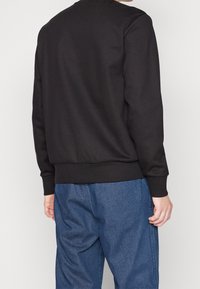 Svart sweatshirt med rund halsringning och ribbade muddar, kombinerad med ljusblå byxor med fiskbensmönster. Avslappnad, ledig passform.