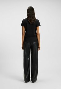 Schwarzes Baumwoll-T-Shirt mit kurzen Ärmeln, kombiniert mit weiten, hochtaillierten schwarzen Hosen aus Kunstleder; glatte Textur und lockere Passform.