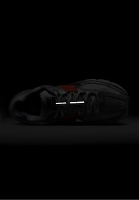 Nike sneaker with a grey mesh upper, orange accents, reflective stripes, and black rubber sole. Laces are threaded through eyelets.