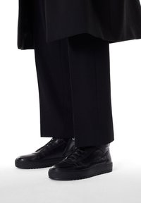 Zapatillas altas de cuero negro con superficie texturizada y suela en capas, que presentan un diseño de cordones y un sutil detalle de marca.