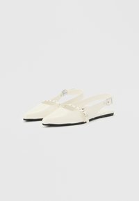 Κρεμ μπεζ μπαλαρίνες με μυτερή μύτη, σχέδιο slingback με λεπτά λουράκια στον αστράγαλο και ασημένιες αγκράφες, σε απλό φωτεινό φόντο.