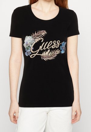 Musta T-paita, jossa on näkyvä "Guess"-logo sinivalkoisin kukkakuosein, lyhyet hihat ja pyöreä kaula-aukko.