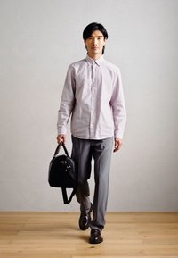 Ljust rosa randig skjorta, grå byxor och bruna skor. Håller en svart läderväska med axelrem och handtag.