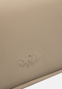 Prodotto in pelle beige con superficie texturizzata e un design in rilievo di due foglie stilizzate in filo contrastante.