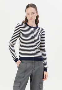 Cardigan navy cu dungi albe, cu guler rotund, închidere cu nasturi și manșete cu nervuri, asortat cu pantaloni cargo gri cu buzunare.