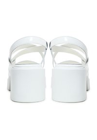 Sandali platform bianchi con finitura lucida, dotati di cinghie incrociate alla caviglia e un tacco spesso per supporto. Texture liscia e design minimalista.