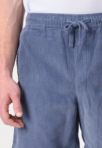 Svetlomodré kordové nohavice s textúrovaným, pruhovaným povrchom. Obsahujú elastický pás s šnúrkou a bočné vrecká.