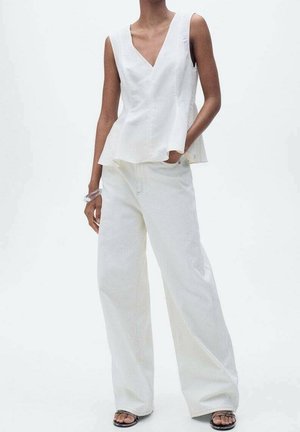 Witte peplum top met een V-hals en witte jeans met wijde pijpen, met een gladde textuur en strakke lijnen, aangevuld met zwarte sandalen.